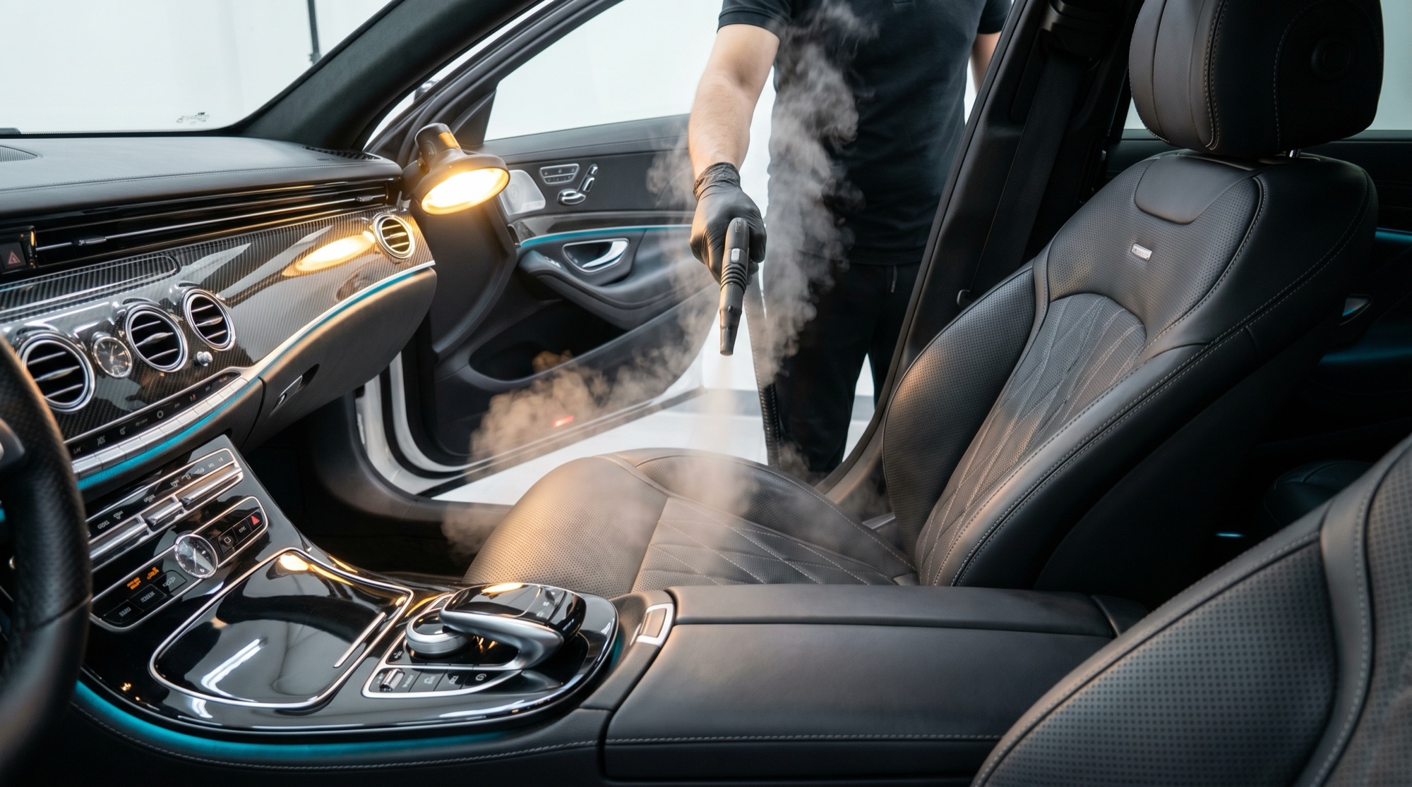 Detailer steam-cleaning a luxury car interior with conditioned black leather seats
